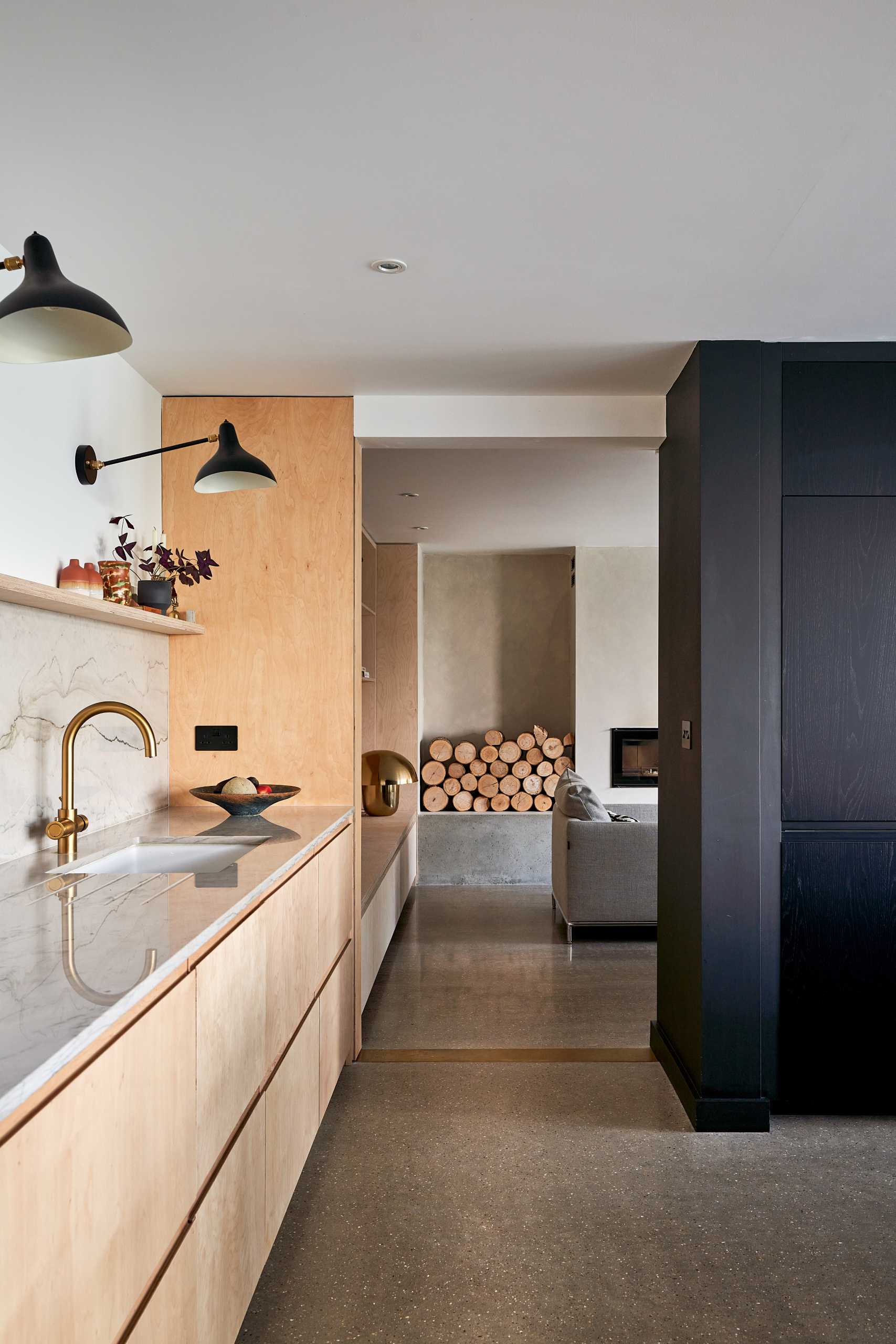 This modern black kitchen has a brass backsplash and an island with shelving for cookery book storage, while plywood has been used for the larder (pantry).