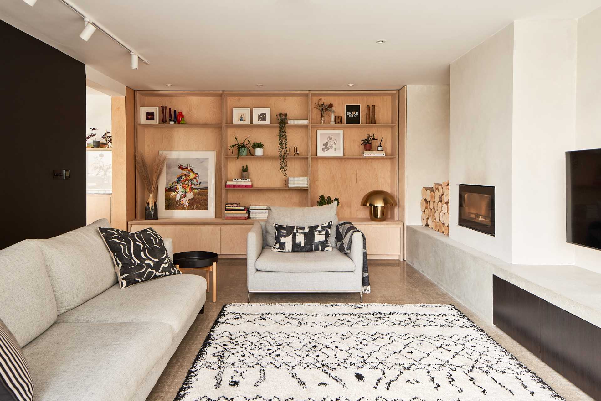 In this living room there's a new fireplace and bench, which can also be used for firewood storage, while a custom wood shelving unit fills a wall, and a black accent wall provides a backdrop for the couch.