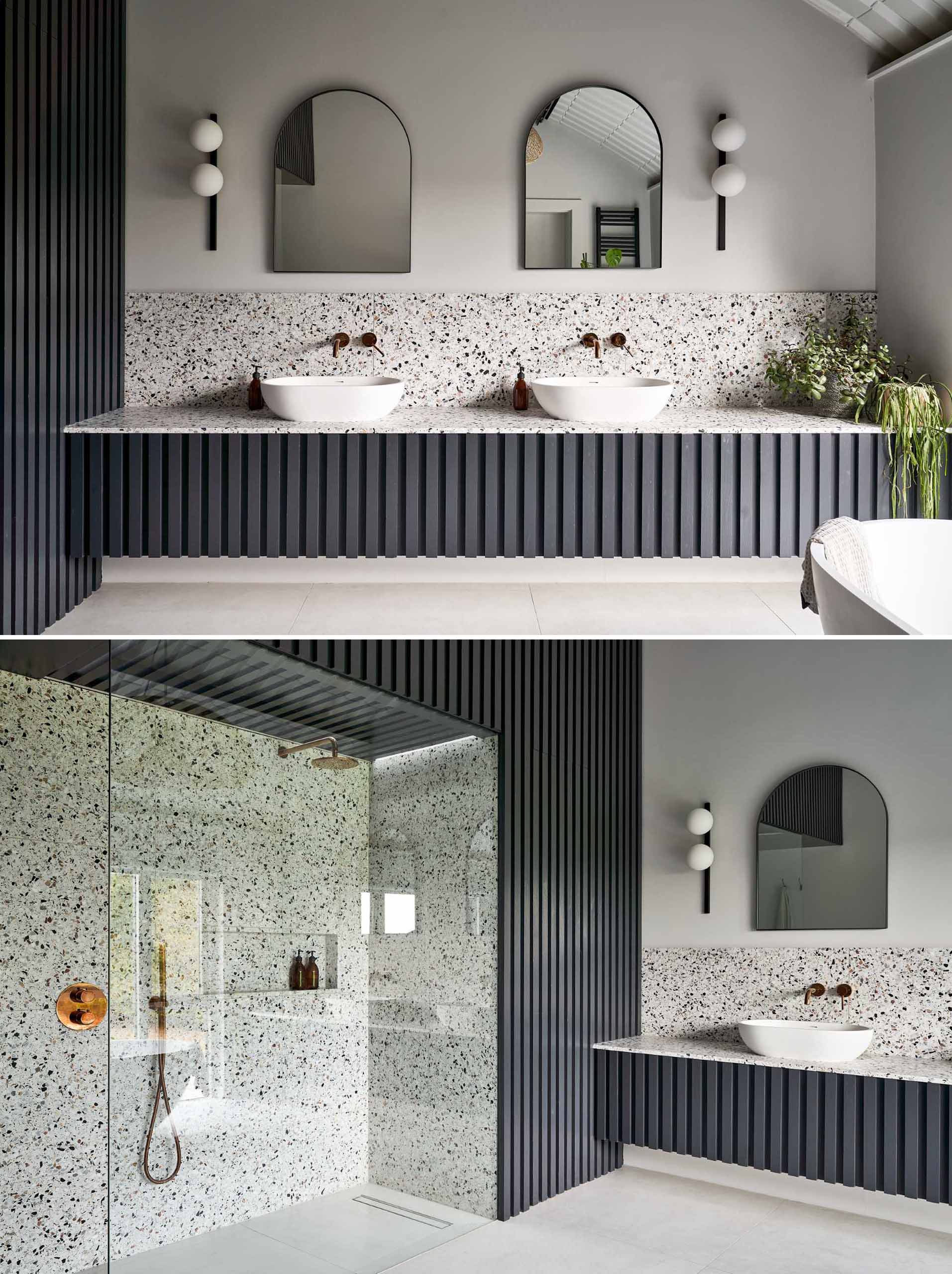 In this modern primary en-suite bathroom, there's a dark double vanity whose design complements the bed headboard, while the shower is recessed into the wall, and the freestanding bathtub is positioned by the window.