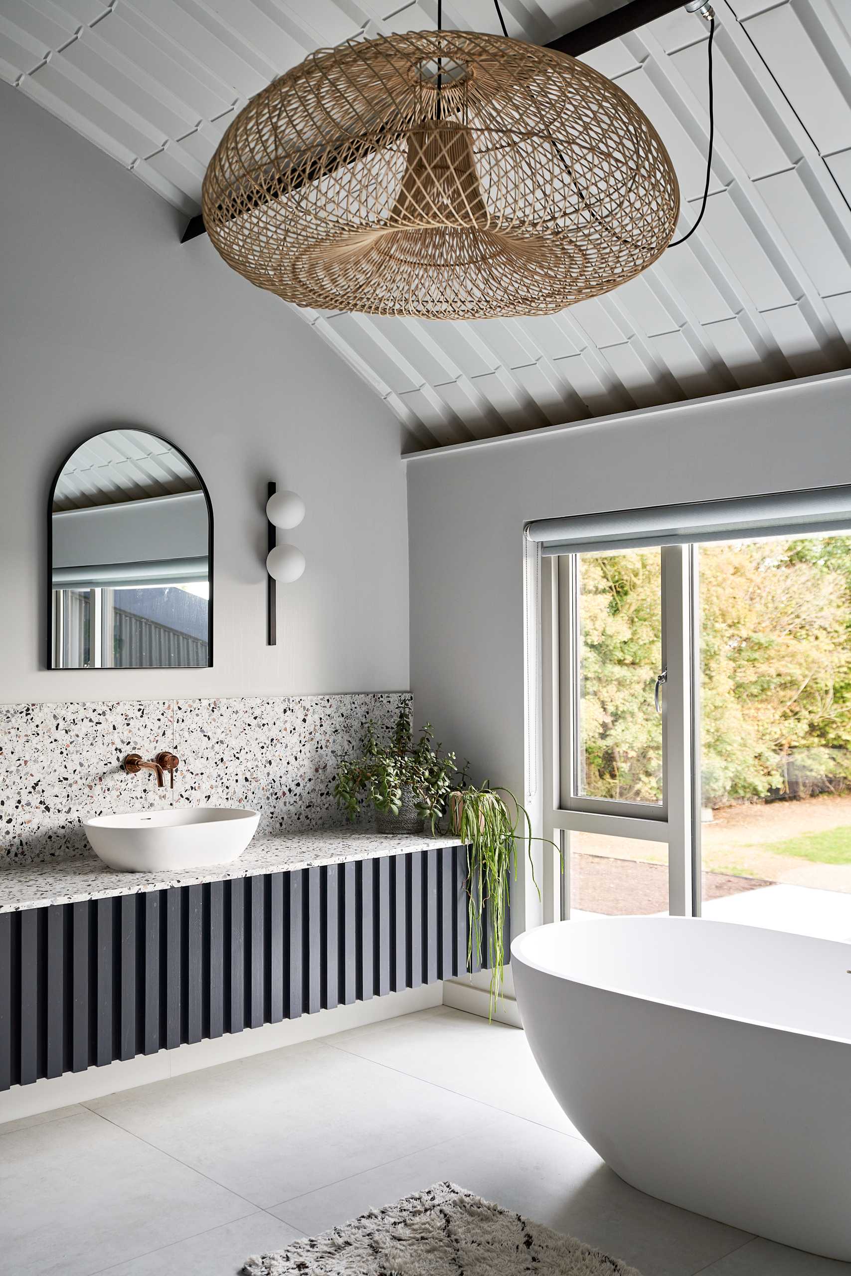 In this modern primary en-suite bathroom, there's a dark double vanity whose design complements the bed headboard, while the shower is recessed into the wall, and the freestanding bathtub is positioned by the window.