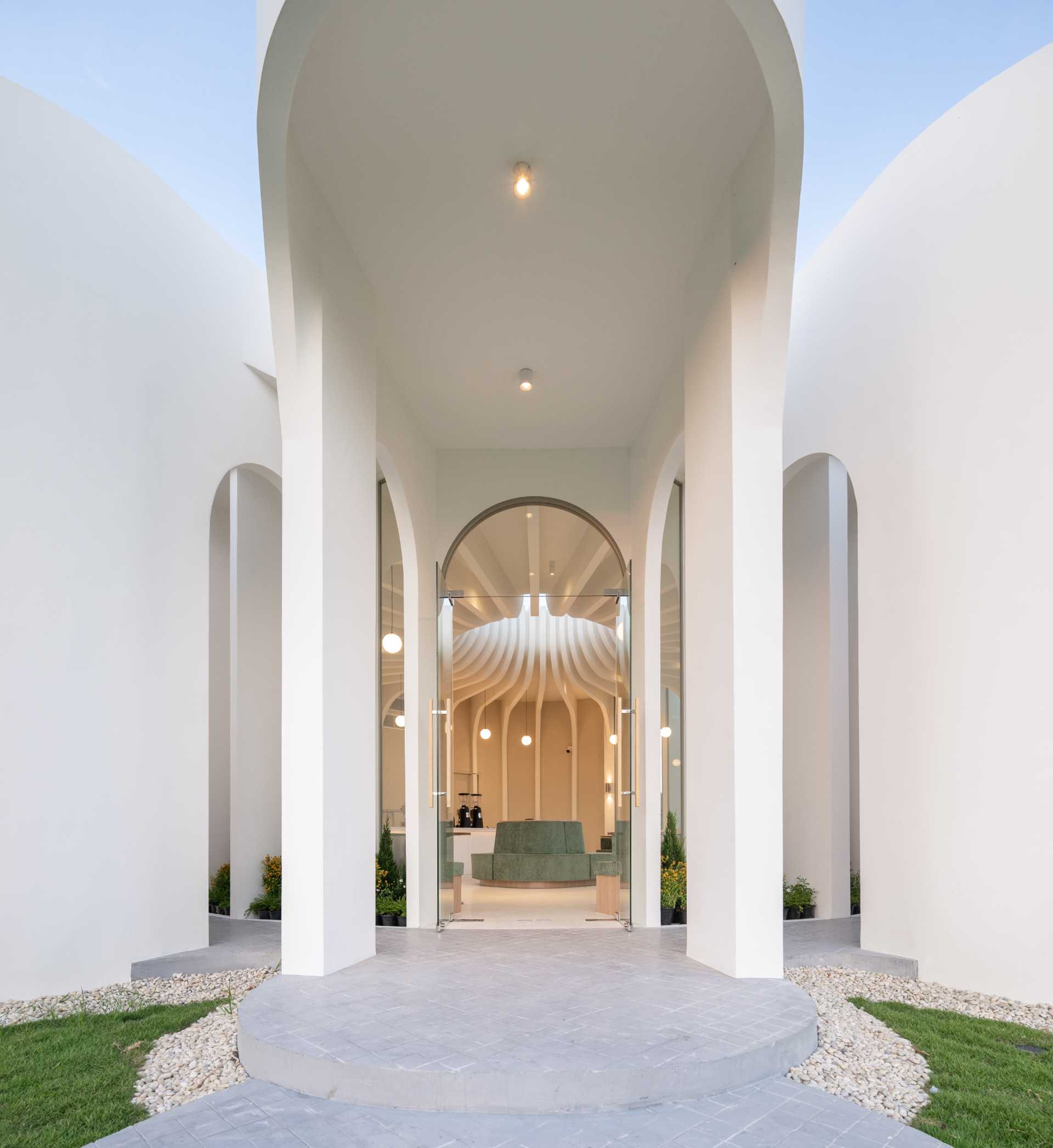 A modern cafe has oversized stepping stones that lead to a grand arched entrance with glass doors.