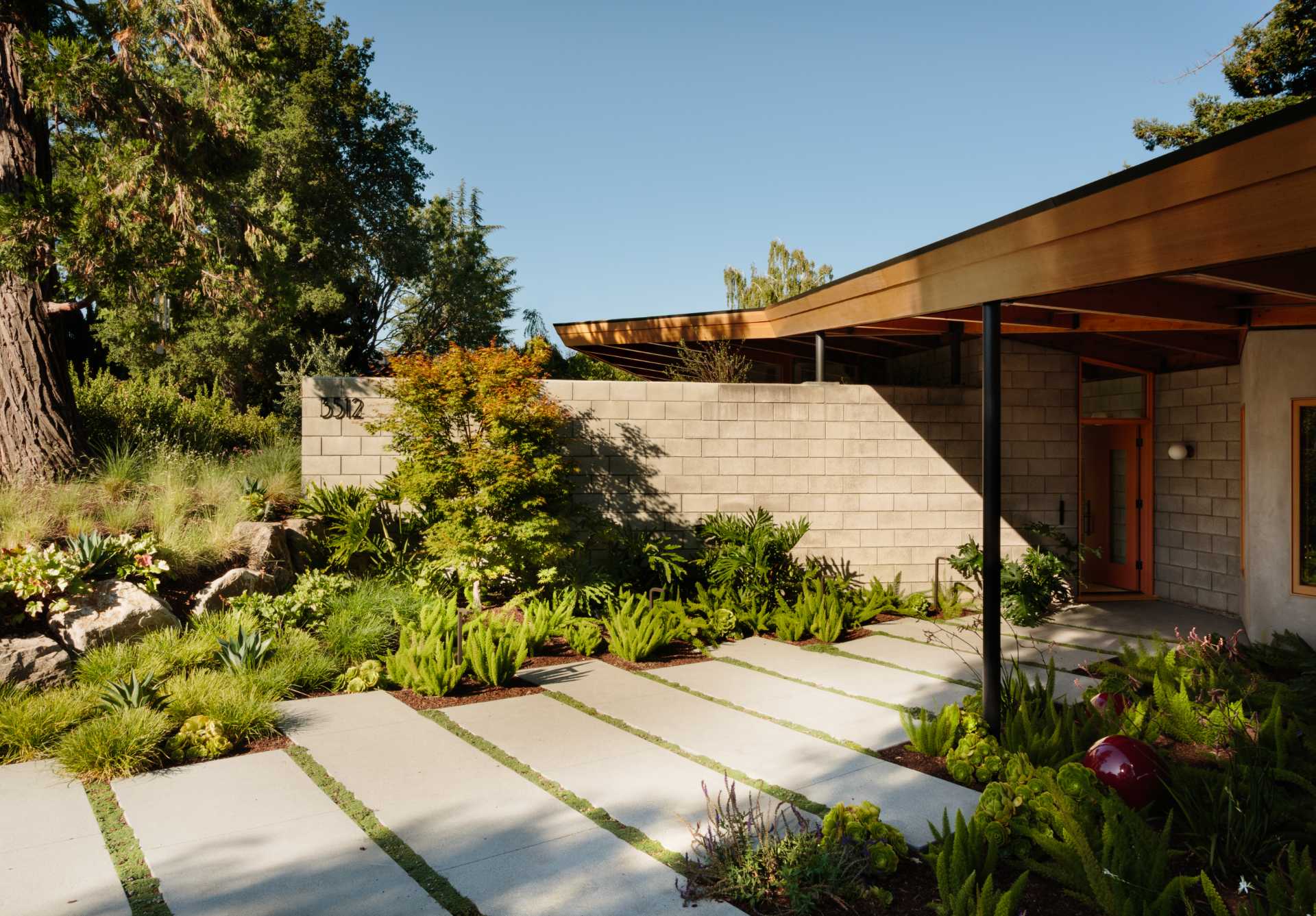 A paved path lined with plants leads to the front door of this renovated mid-century modern home.