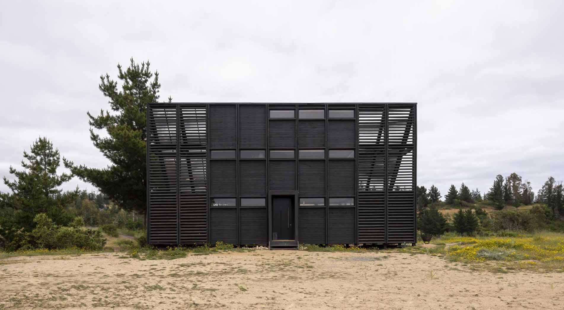 A small wedge-shaped home with a black exterior that's located on the windy beach of Matanzas, Chile.