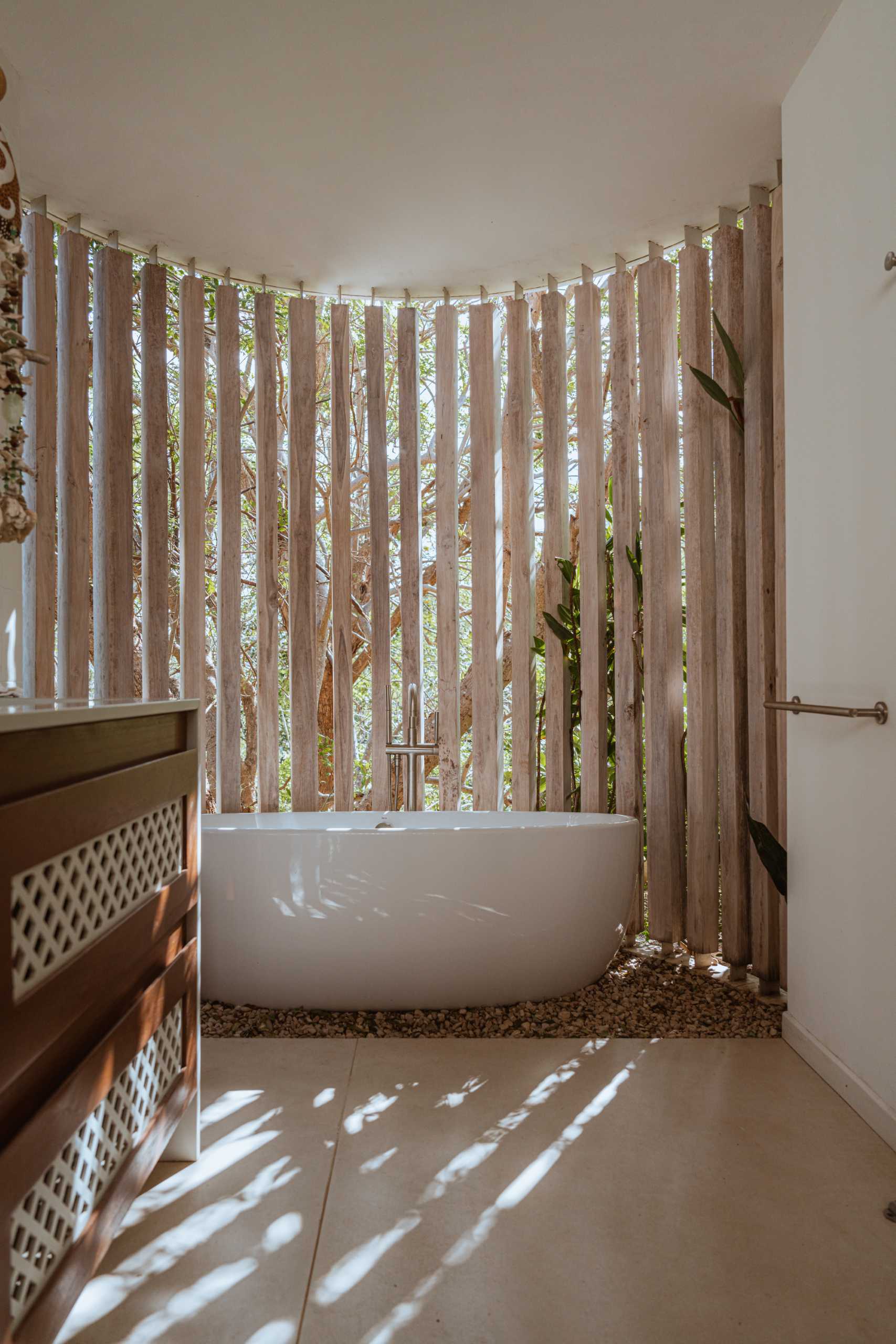 A modern bathroom with a freestanding bathtub positioned by a curved partition, making it feel like your bathing outdoors.