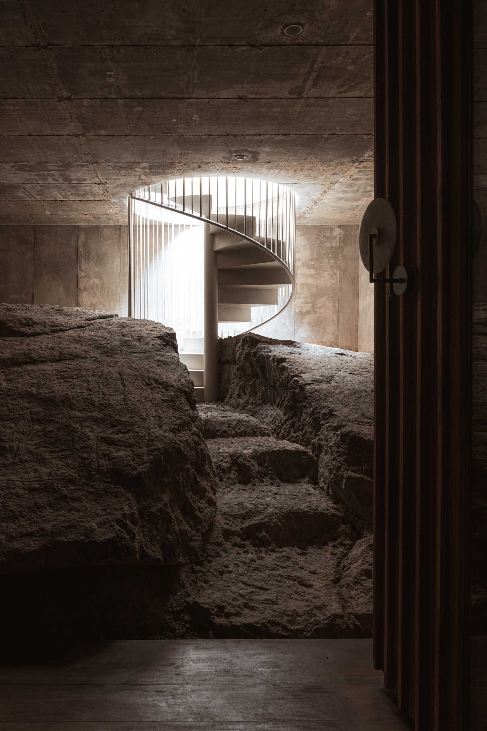 A spiral staircase leads down to a basement with steps carved out of stone.