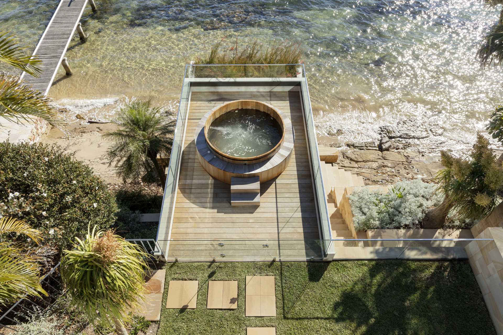 A modern waterfront home has a boatshed with a timber rooftop spa.