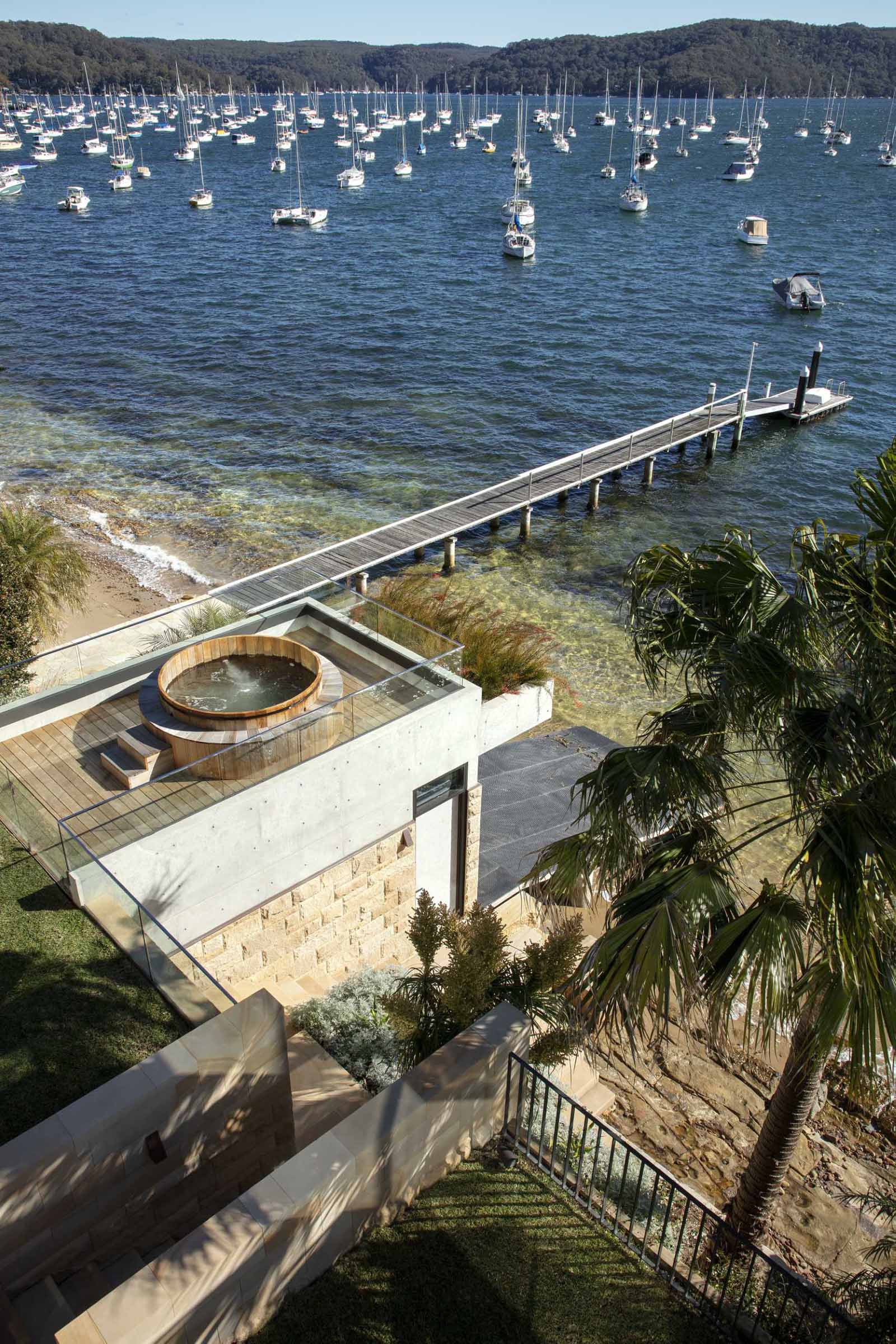 A modern waterfront home has a boatshed with a timber rooftop spa.