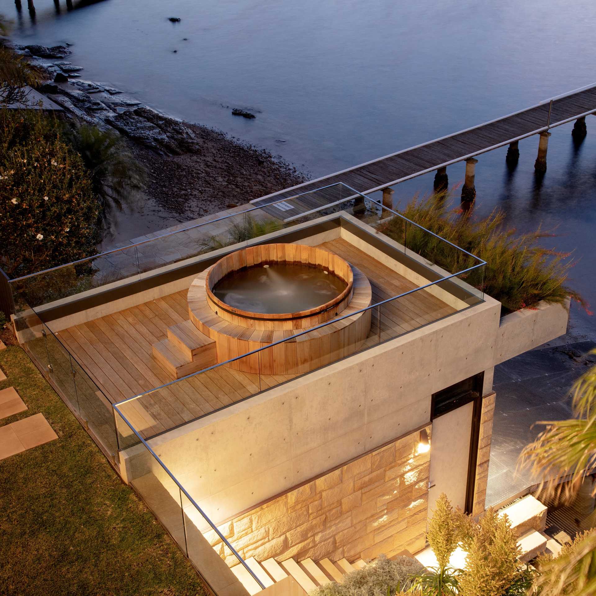 A modern waterfront home has a boatshed with a timber rooftop spa.