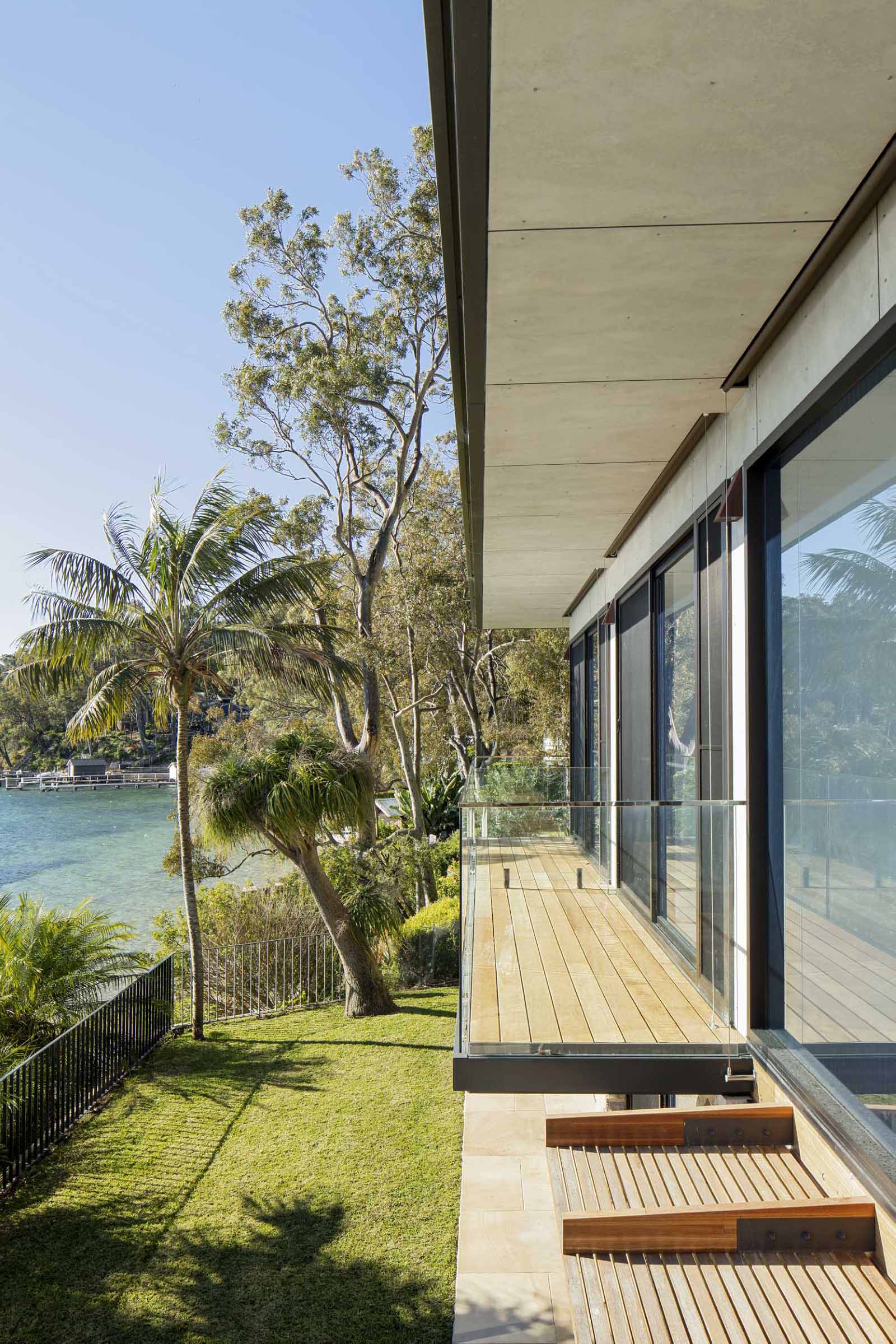 A modern waterfront home features a lightweight floating roof and timber stacking doors that slide away to open the living areas completely to the external terraces and verandah.