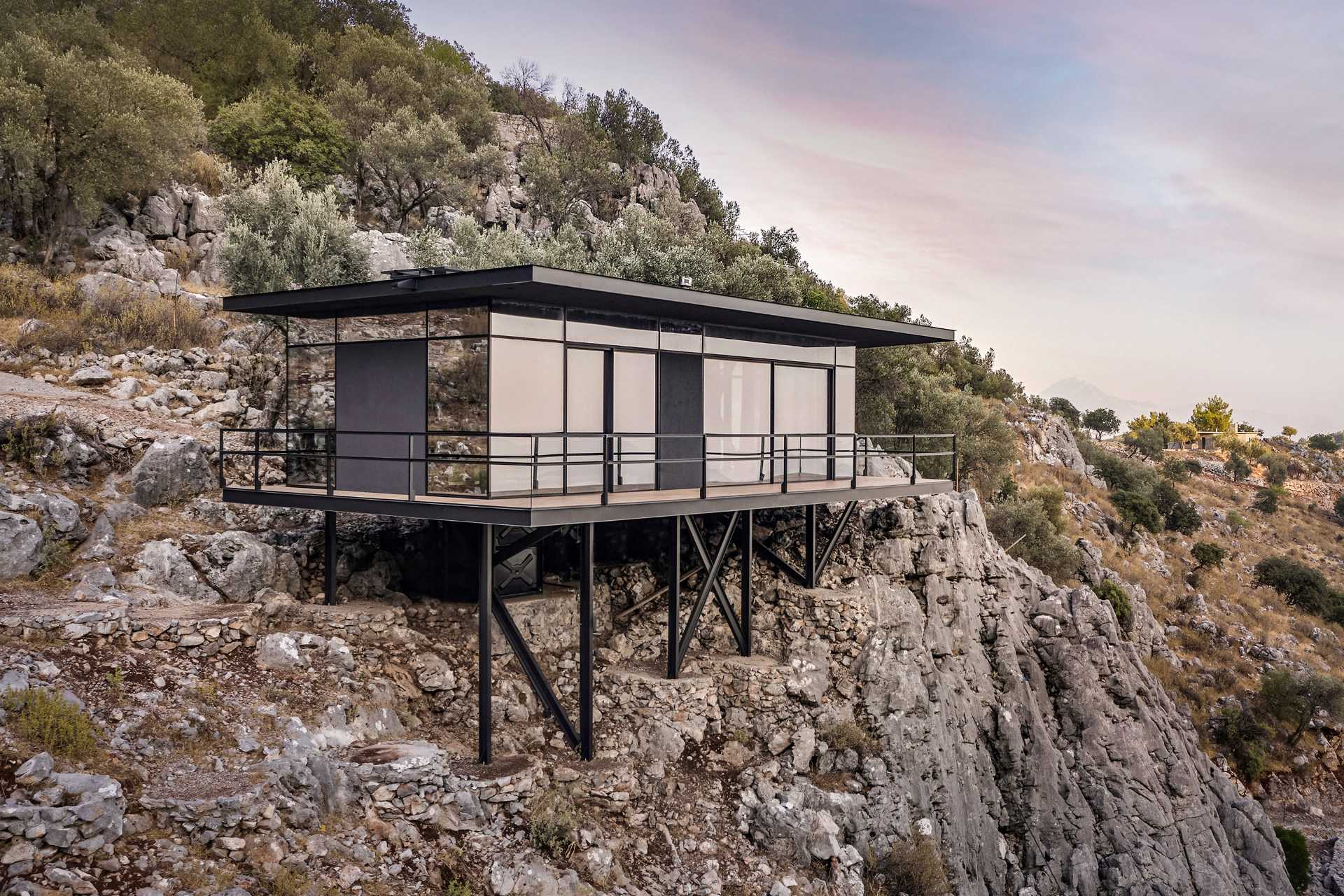 A small one-bedroom cabin with an open plan interior, is made from steel construction and a glass facade.