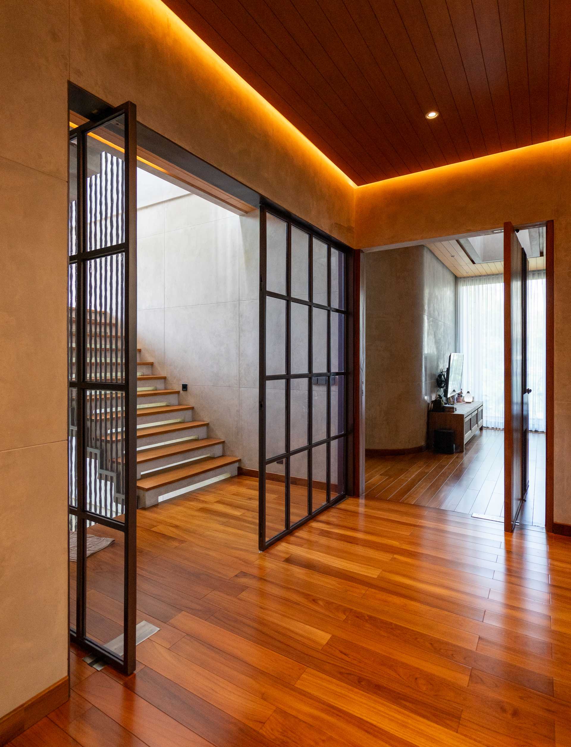 A modern home with wood floors and a pivoting black metal framed glass door.